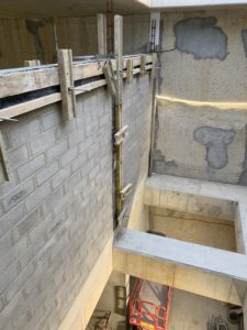 Voile en parpaings pleins avec poteaux et chaînages coffrées et coulés en place, bétonnage du chaînage horizontal en cours