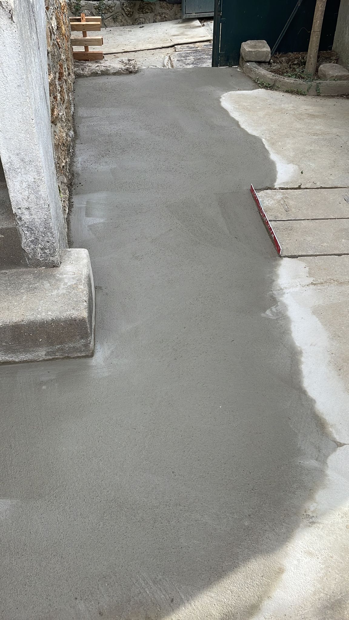 BATI-IDF dalle béton fraîchement coulée et lissée au pied du mur en meulière, finition propre des travaux de reprise en sous-œuvre post-sécheresse à Antony (92).