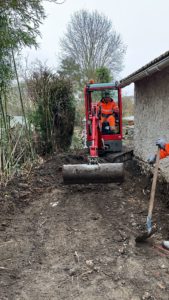 BATI-IDF équipe en plein terrassement périphérique en pied du pavillon, mini-pelle au travail pour ouvrir la tranchée d'accueil du dispositif anti-sécheresse — Boissy-sans-Avoir (78).