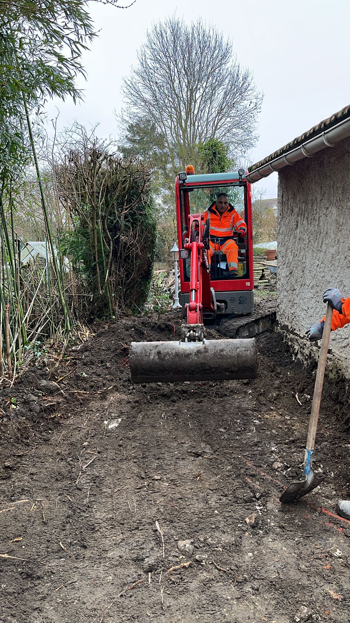 BATI-IDF équipe en plein terrassement périphérique en pied du pavillon, mini-pelle au travail pour ouvrir la tranchée d'accueil du dispositif anti-sécheresse — Boissy-sans-Avoir (78).