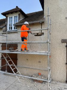 BATI-IDF compagnon sur échafaudage en train de scier l'engravure horizontale dans la maçonnerie en pierre pour la mise en place d'un chaînage BA — pavillon Boissy-sans-Avoir (78).