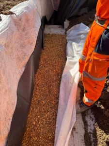 BATI-IDF complexe drainant en pose dans la tranchée : géomembrane PVC, cailloux drainants 20/40 et géotextile enveloppant — Boissy-sans-Avoir (78).