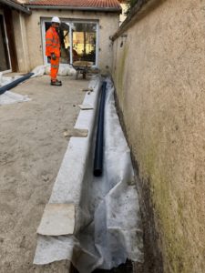 BATI-IDF drain souple posé dans la tranchée de drainage périphérique avec géotextile déployé, compagnon BATI-IDF en pied du pavillon — Boissy-sans-Avoir (78).