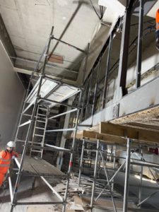 BATI-IDF compagnon en pleine déconstruction soignée — laine de roche déjà démontée sur une partie, échafaudages en place — Centre de tri La Poste, Paris 17e.