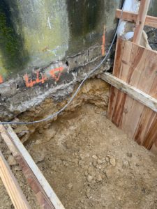 BATI-IDF fouille en pied du mur béton existant et repères orange marquant les emplacements des trous de scellement pour la liaison des aciers — chantier RSO Orly (94).