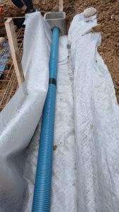 BATI-IDF drain souple bleu posé sur le géotextile dans la tranchée de drainage périphérique, prêt à être recouvert de cailloux drainants — Ouges (21).