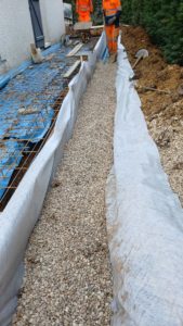 BATI-IDF mise en place des cailloux drainants autour du drain, équipe BATI-IDF au travail en pied du pavillon, futur trottoir ferraillé à gauche — Ouges (21).