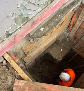 BATI-IDF compagnon en gilet orange et casque blanc au fond d'une fouille blindée par planches bois, vue plongeante montrant la profondeur de l'excavation — Saint-Lô (50).